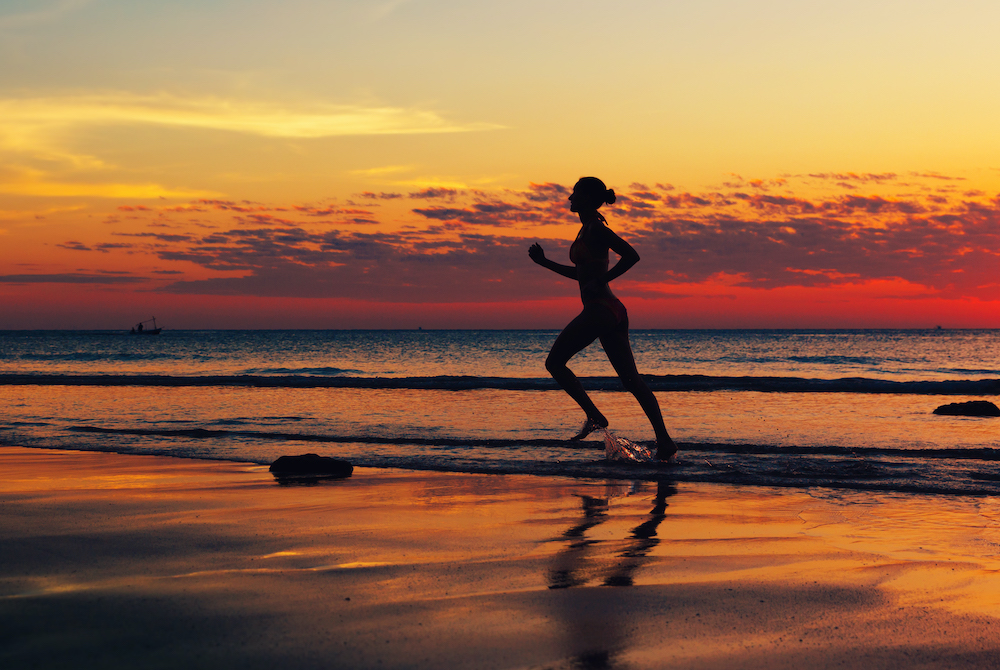 Mujer en plan de renovación, corriendo en la playa al atardecer